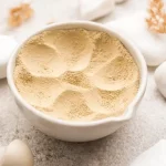 Sojas proteīna pulveris baltā bļodā uz gaiša dabīga akmens fona