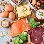 Produkti, kas satur aminoskābes – olas, lasis, gaļa, biezpiens, pākšaugi un rieksti uz virtuves galda.