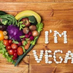 Kas ir vegāns – sirds forma no augļiem un dārzeņiem ar uzrakstu “I’m vegan” pupiņās uz koka virsmas