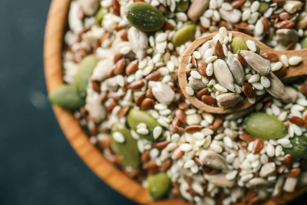 Dažādu sēklu maisījums koka bļodā ar karoti – saulespuķu, sezama, linsēklas un ķirbju sēklas