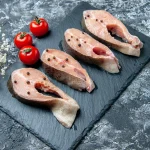 Svaigas laša šķēles uz melna akmens dēlīša ar pipariem – bagātīgs valīna avots.